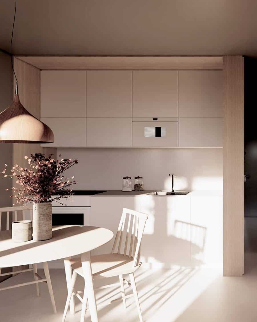 Minimalist kitchen with white cabinets, a round table, white chairs, and a pendant light; sunlight casts shadows on the floor