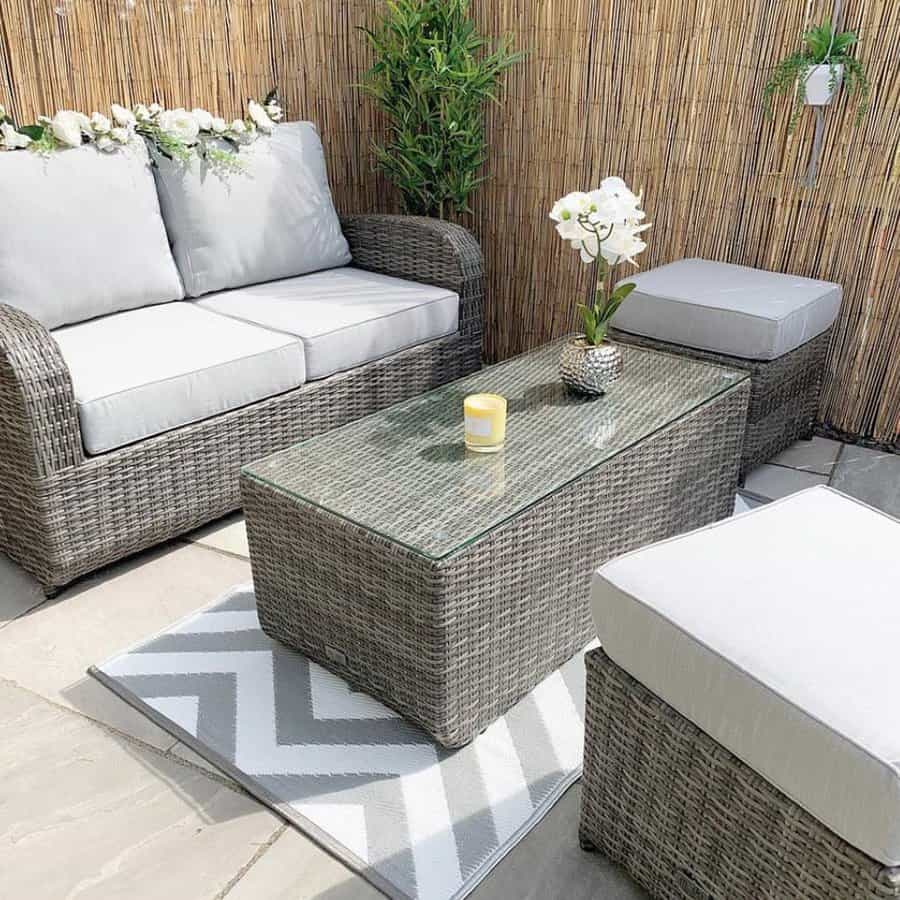 Stylish outdoor patio with gray wicker furniture, white cushions, a glass-top table, candle, orchid, and bamboo privacy screen