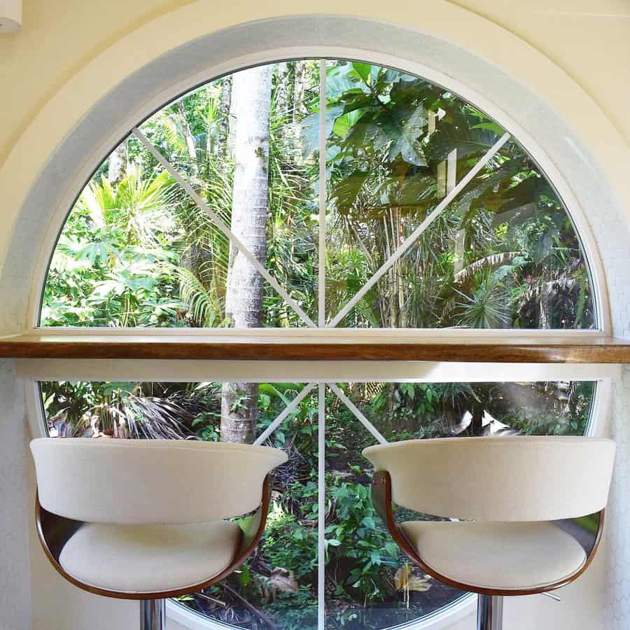 Serene window breakfast bar with a sleek wooden countertop, elegant white barstools, and a breathtaking view of lush tropical greenery