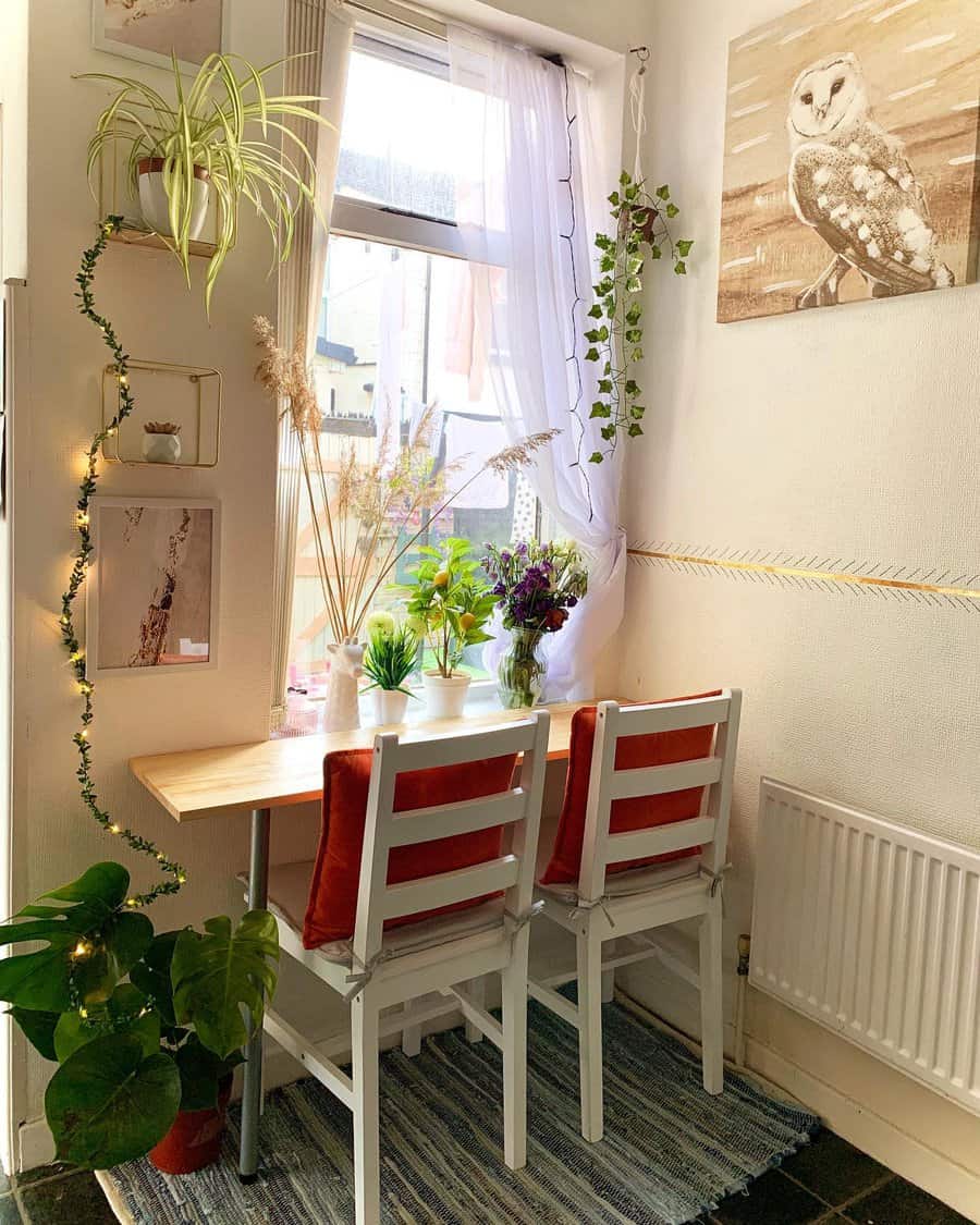 Charming window breakfast nook with a wooden table, cozy white chairs, lush greenery, soft curtains, and warm fairy lights for a relaxing ambiance