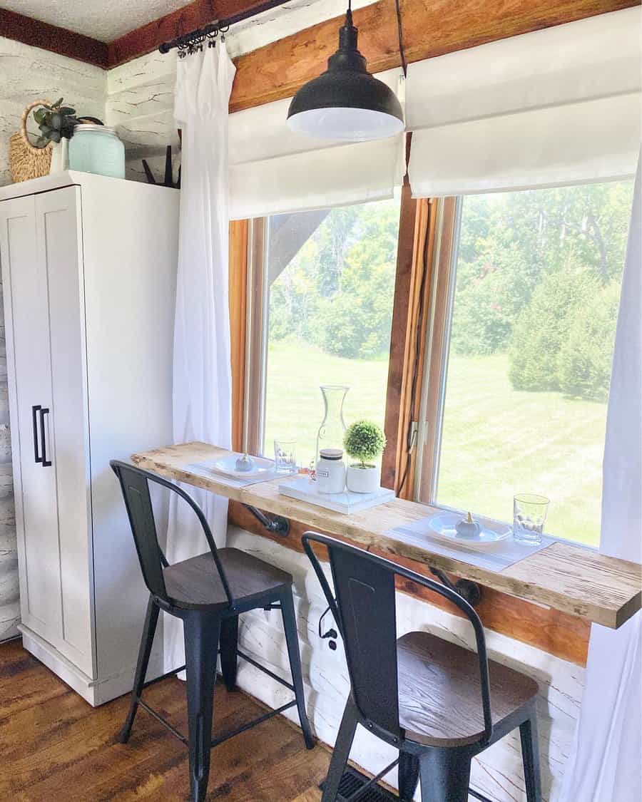 Cozy breakfast nook with a wooden bar table, two metal chairs, pendant light, and window view of greenery