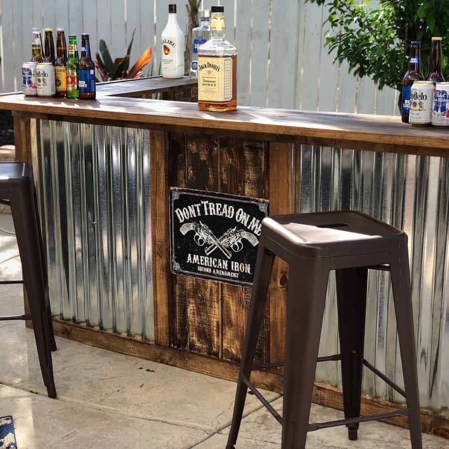 Outdoor bar with metal and wood design, surrounded by stools, "Don’t Tread on Me" sign and bottles on the counter