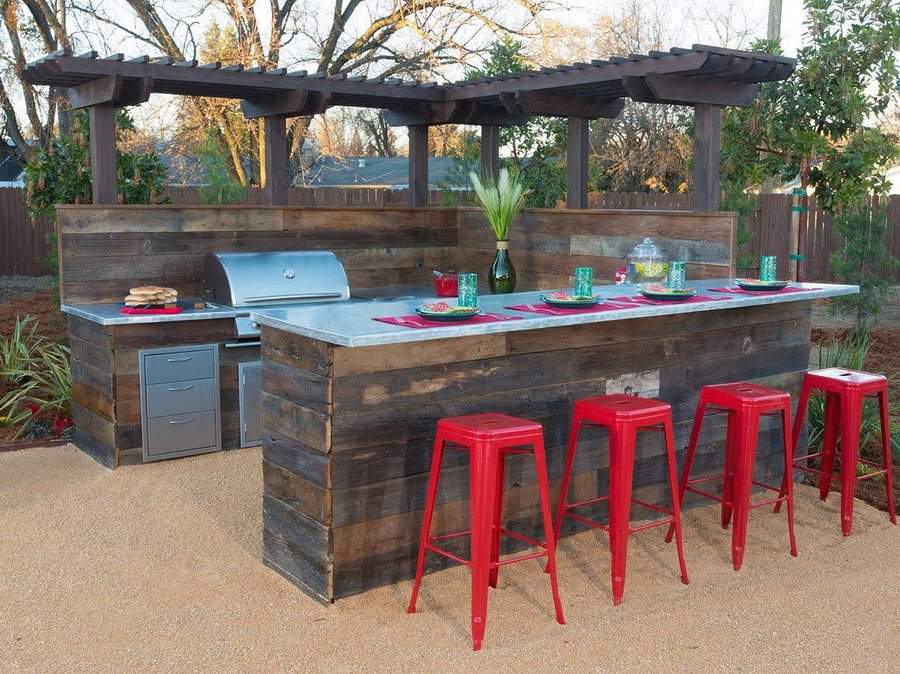 Stylish outdoor bar with a rustic wood finish, pergola, built-in grill, and vibrant red stools, perfect for entertaining guests