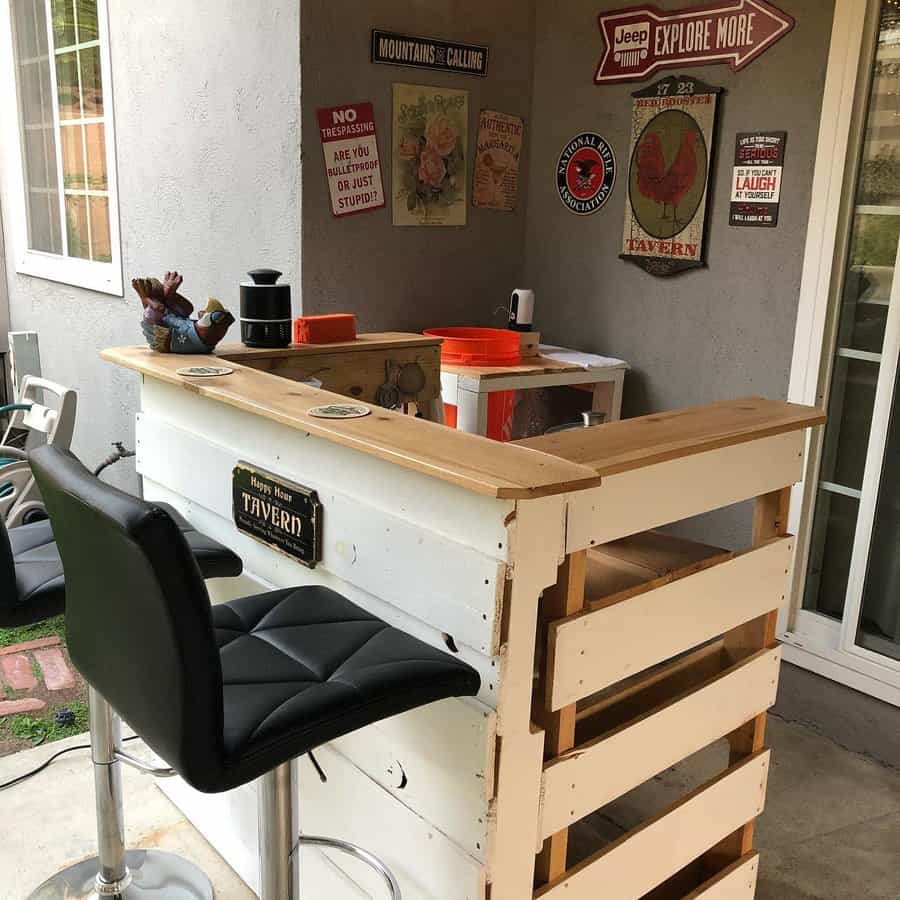 DIY patio bar with wooden counter, two black bar stools, wall signs, and decor; located on a covered porch