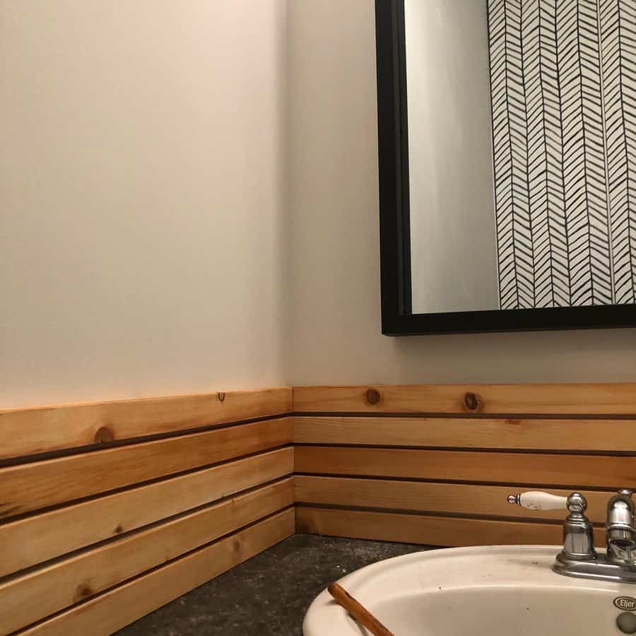 Rustic bathroom with horizontal wood slat backsplash, granite countertop, vintage-style faucet, and a black-framed mirror for a cozy cabin vibe.