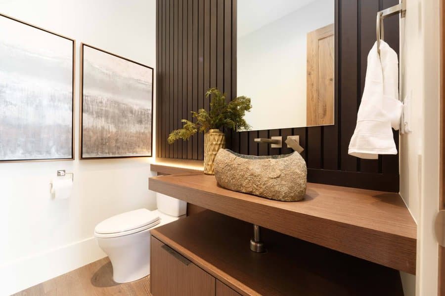 Modern rustic bathroom with vertical dark wood slat backsplash, floating wood vanity, stone vessel sink, and warm accent lighting.