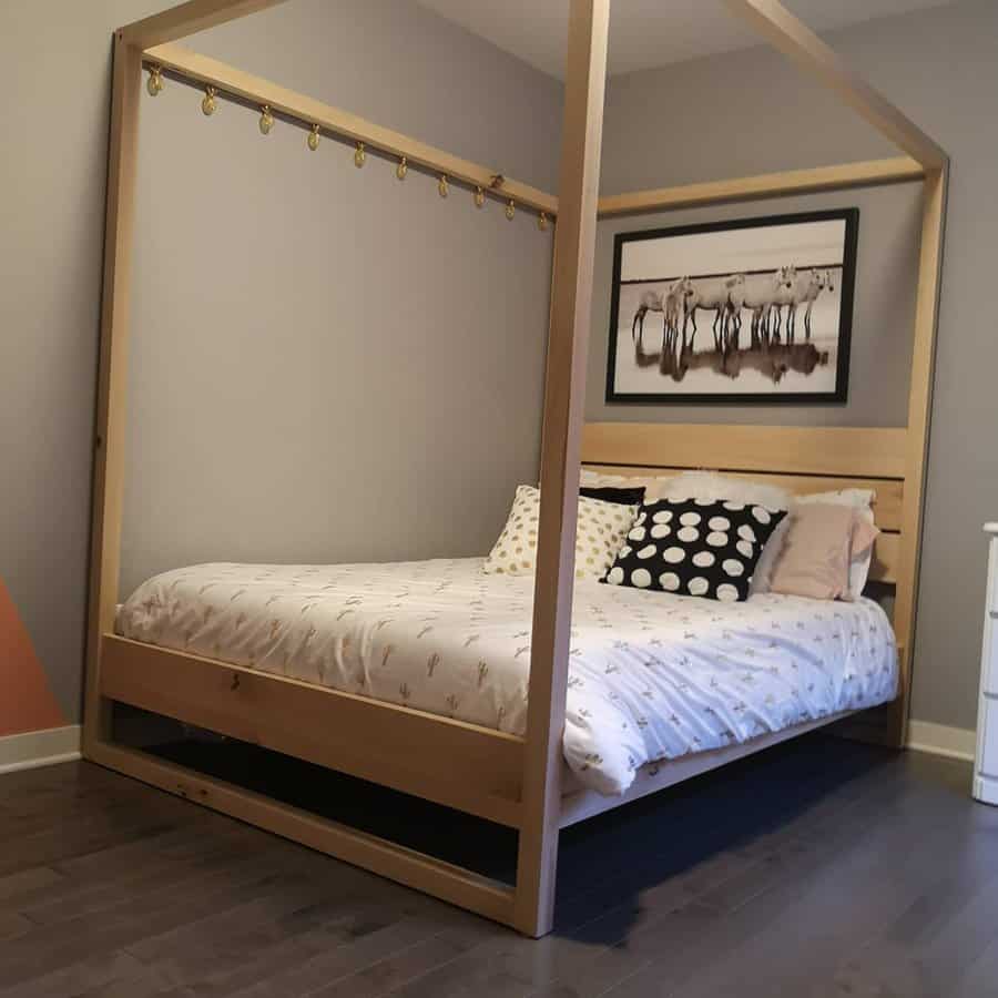 Minimalist wood canopy bed with a sleek frame, neutral bedding, and polka dot pillows, creating a cozy and modern bedroom space