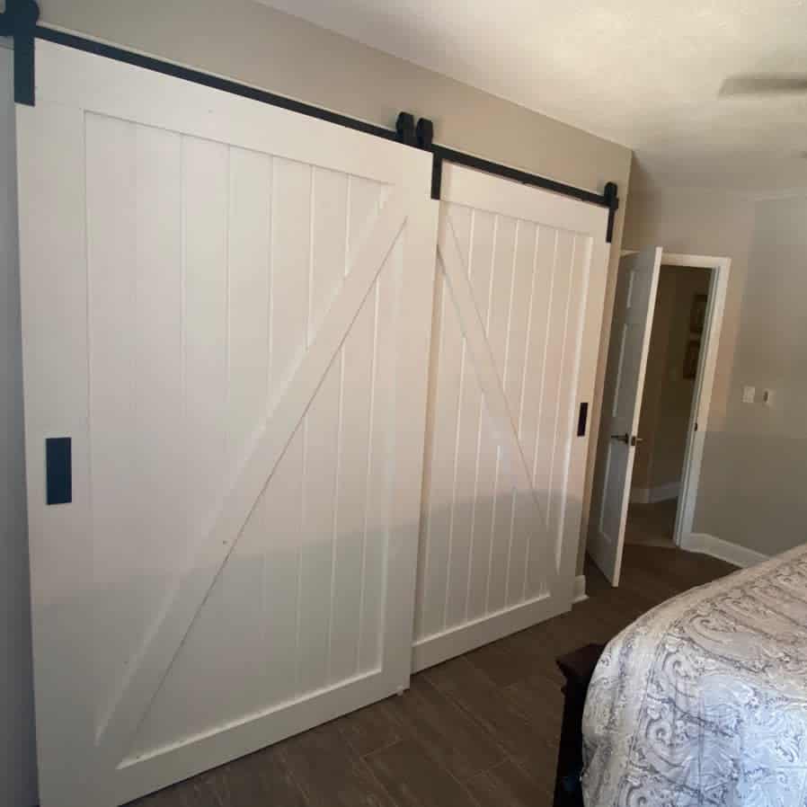 White double barn-style sliding closet doors with black hardware bring a classic farmhouse touch to a cozy bedroom with neutral tones.