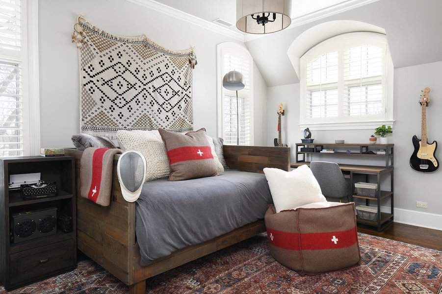 Rustic wooden daybed with cozy gray bedding, Swiss-inspired pillows, and a woven wall hanging, creating a warm and stylish retreat