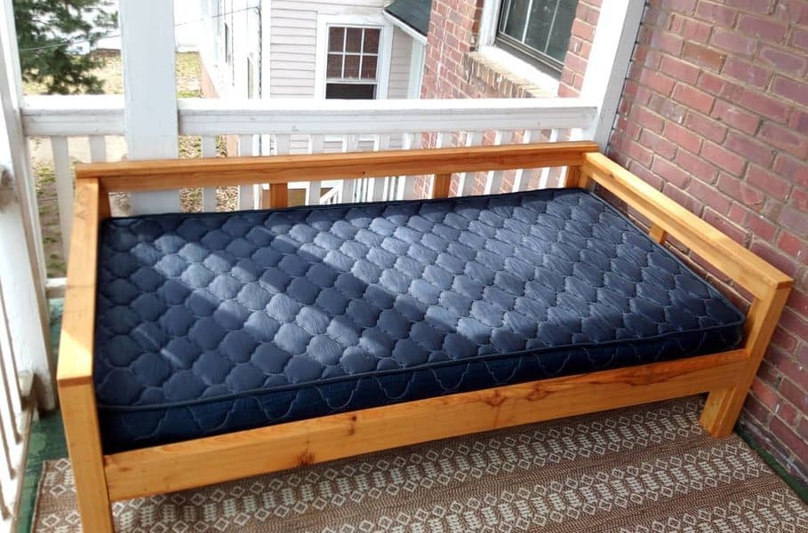 Simple wooden daybed with a sturdy frame and navy quilted mattress, creating a cozy and functional outdoor seating space on a small porch