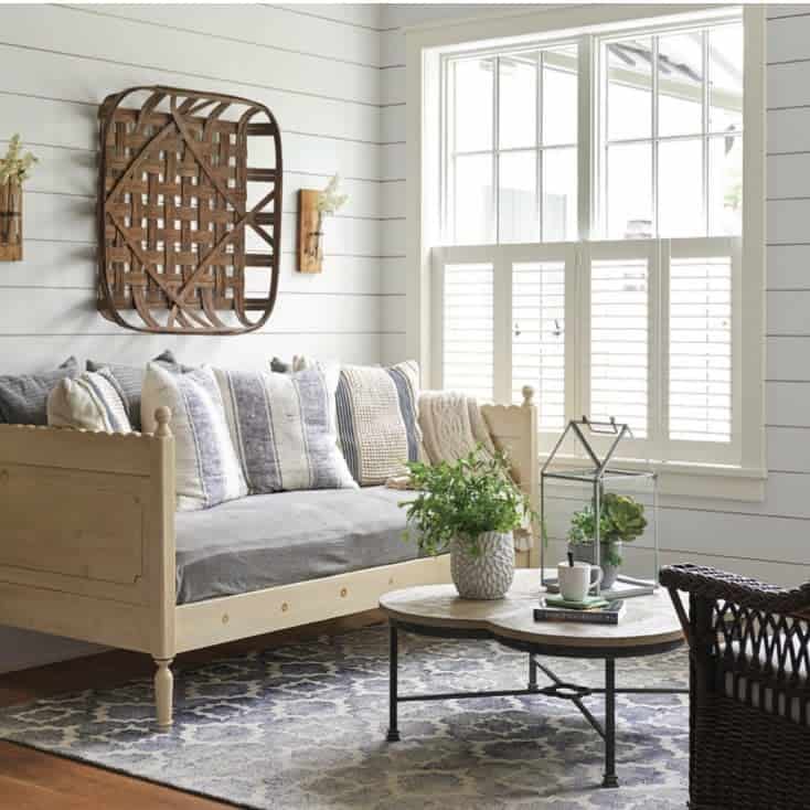 Farmhouse-style wooden daybed with soft gray cushions, striped pillows, and shiplap walls, creating a cozy and inviting living space