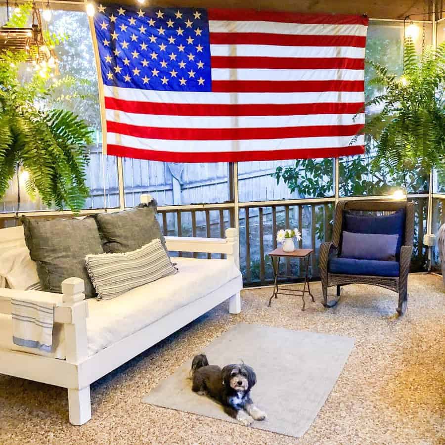 Rustic white wooden daybed with cozy cushions, a patriotic American flag backdrop, and string lights, creating a charming outdoor lounge space