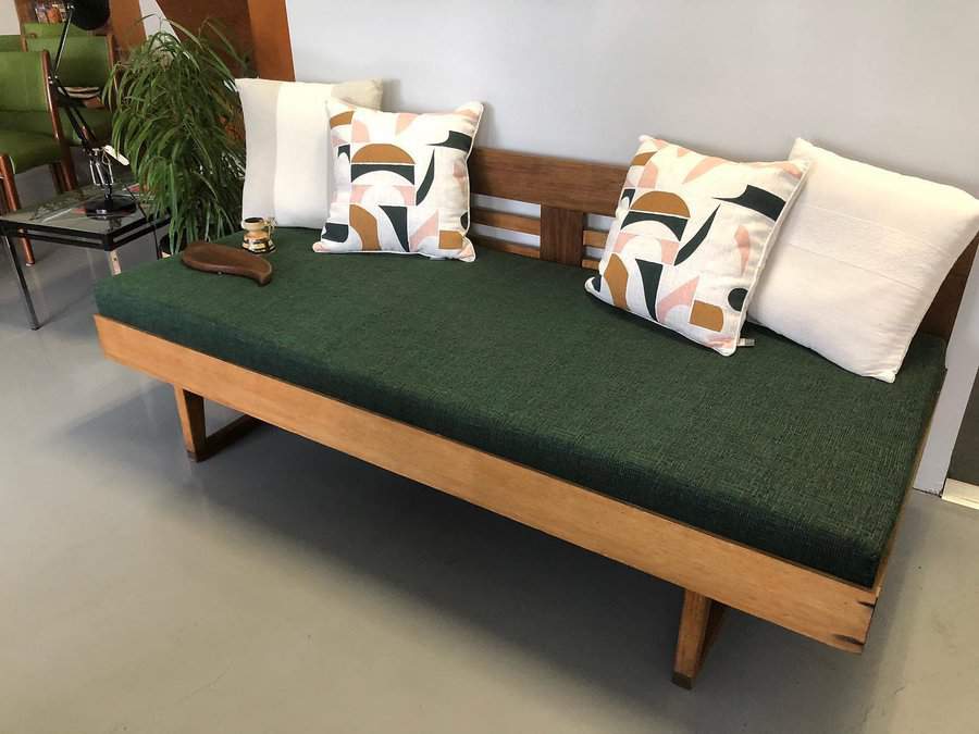 Wooden daybed with green cushion, featuring patterned pillows and a plant nearby, placed in a modern room setting