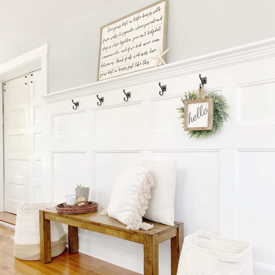 Entryway with a wooden bench, white pillows, hooks on the wall, a "hello" sign with greenery, and a framed quote above