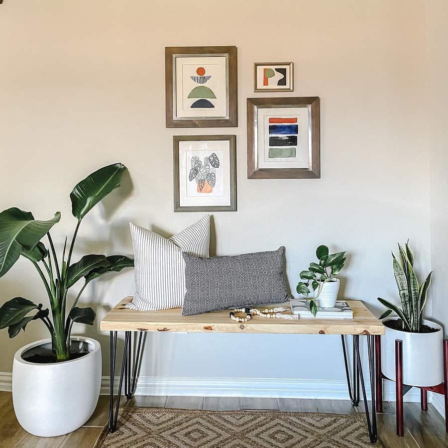 Modern entryway with a wooden bench, throw pillows, potted plants, and colorful abstract art on the wall