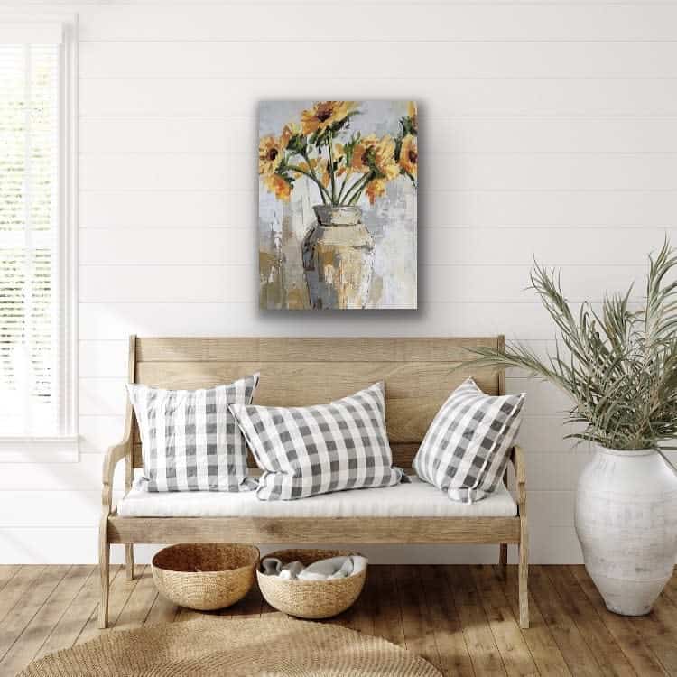 Warm farmhouse entryway with a wooden bench, buffalo check pillows, woven baskets, and sunflower artwork, creating a cozy and inviting space