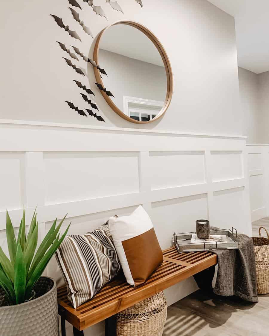 Entryway with a wooden bench, pillows, a mirror, bat decorations, a plant, and storage baskets in neutral tones create a cozy ambiance