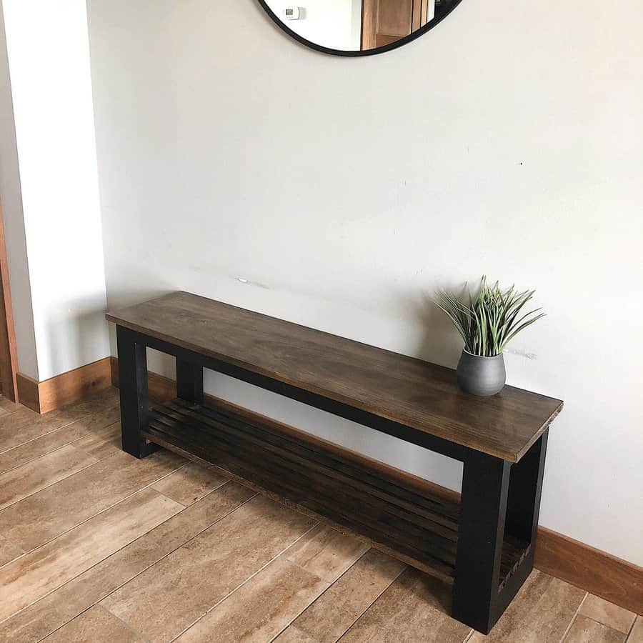 Wooden bench with a potted plant next to a wall-mounted round mirror in a hallway