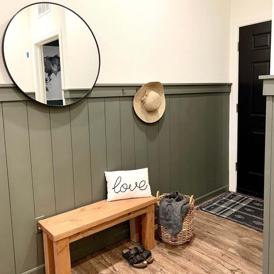 Cozy entryway with a wooden bench, sage green paneling, a round mirror, and woven accents, creating a warm and inviting rustic charm