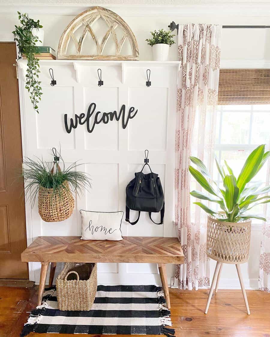 Bright farmhouse entryway with a wooden bench, black-and-white decor, greenery, and a welcoming sign, creating a cozy and stylish space