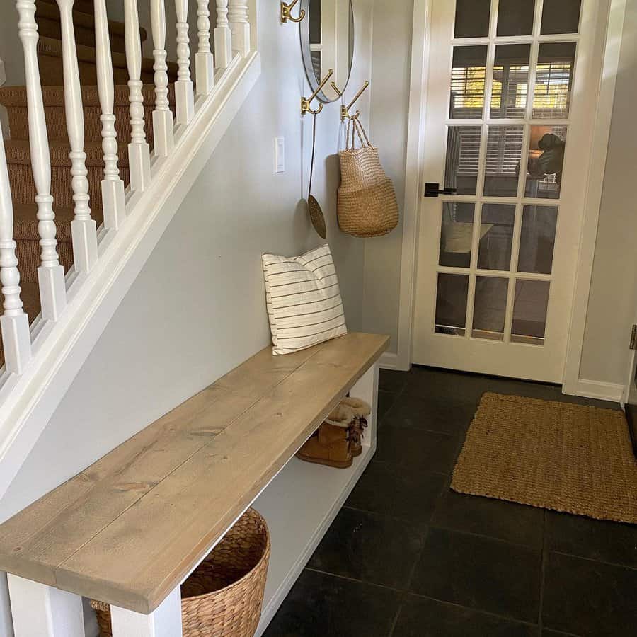 Entryway with wooden bench, striped cushion, baskets, mirror, coat hooks, glass-paned door, and staircase with white railing