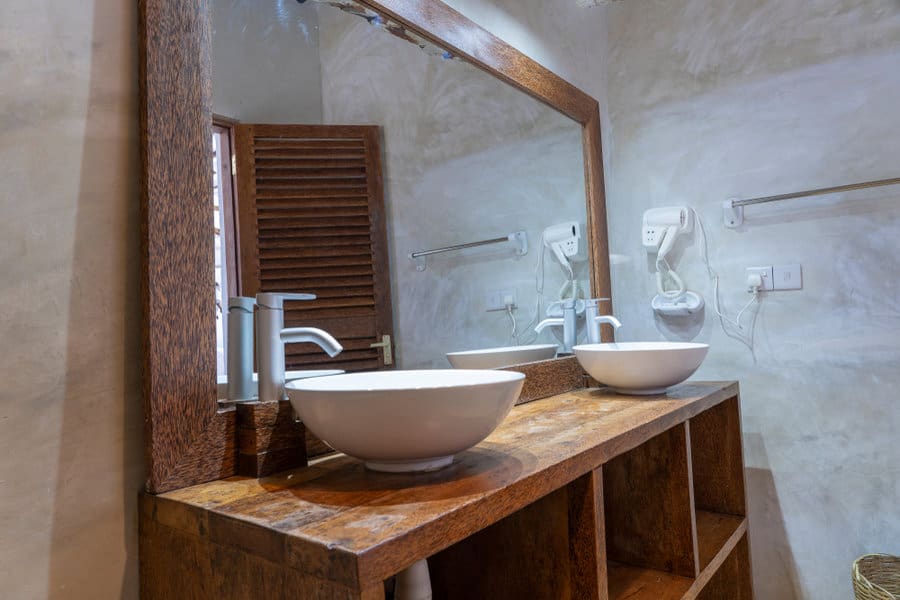 Modern bathroom with two white vessel sinks on a wooden vanity, large mirror, wall-mounted hairdryers, and open shelving