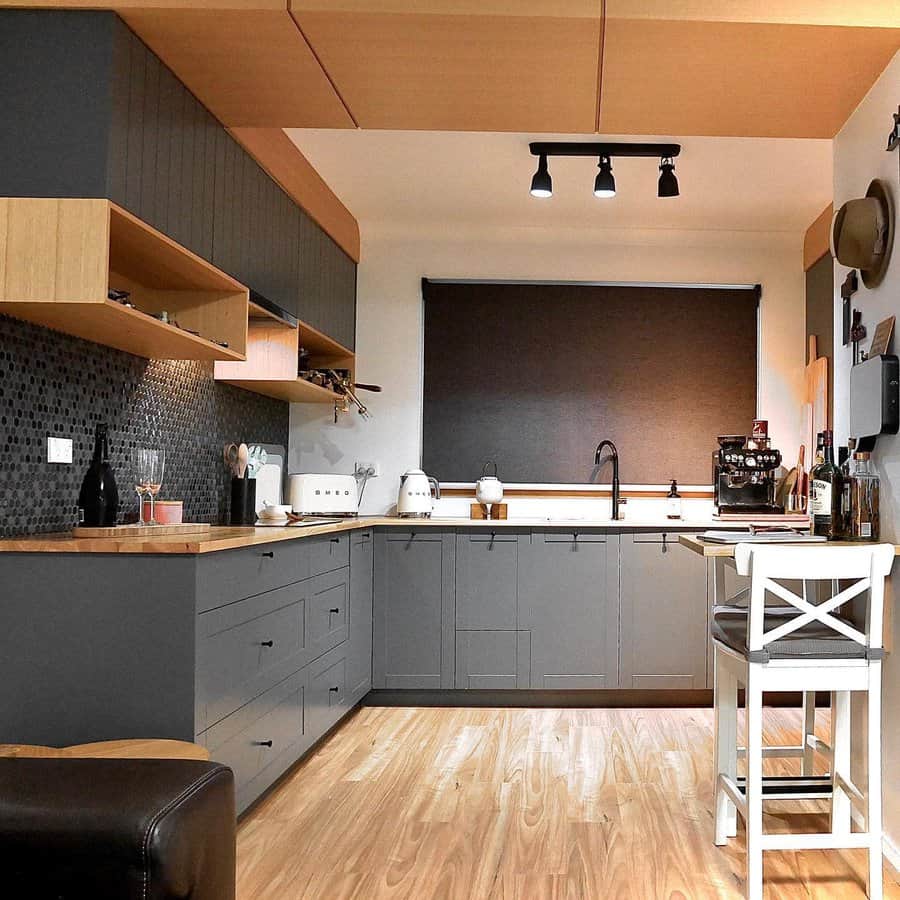 Light wood flooring adds warmth to this modern kitchen, complementing dark cabinetry, wood accents, and a bold black backsplash for a stylish contrast