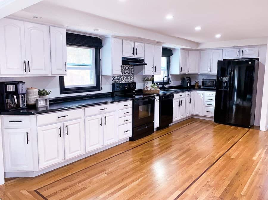 Polished hardwood flooring with decorative inlays enhances this black-and-white kitchen, adding warmth and contrast to the classic cabinetry and modern appliances