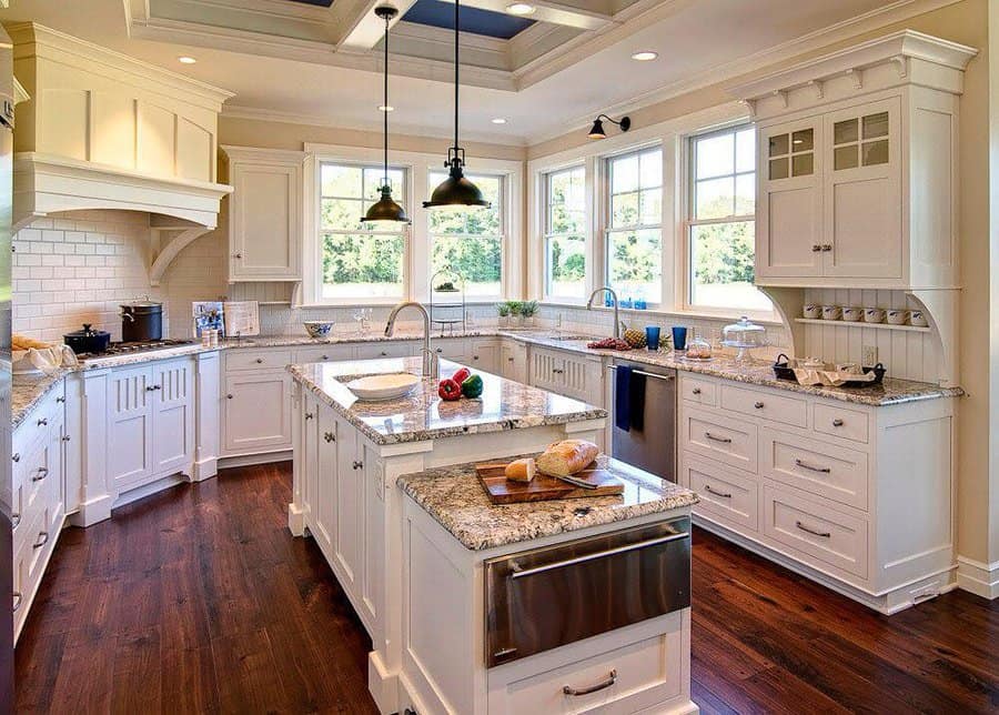 Rich hardwood flooring adds warmth and elegance to this bright farmhouse kitchen, complementing white cabinetry, granite countertops, and natural light