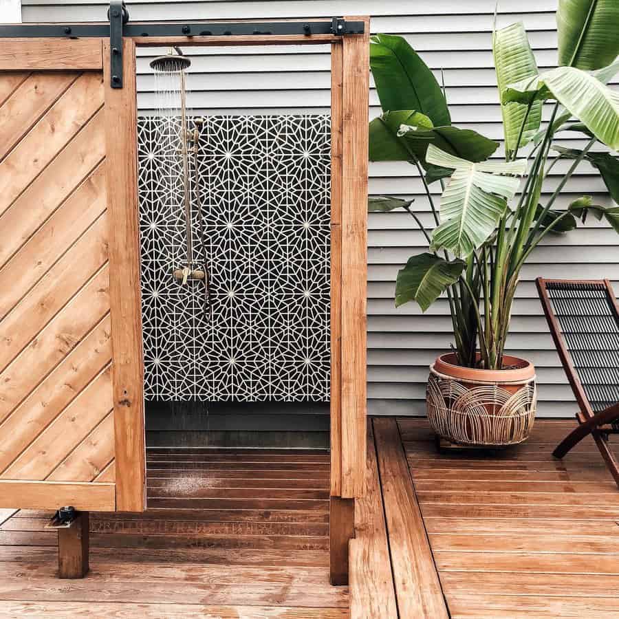 Wooden outdoor shower with patterned privacy screen, tropical plants, and wooden deck