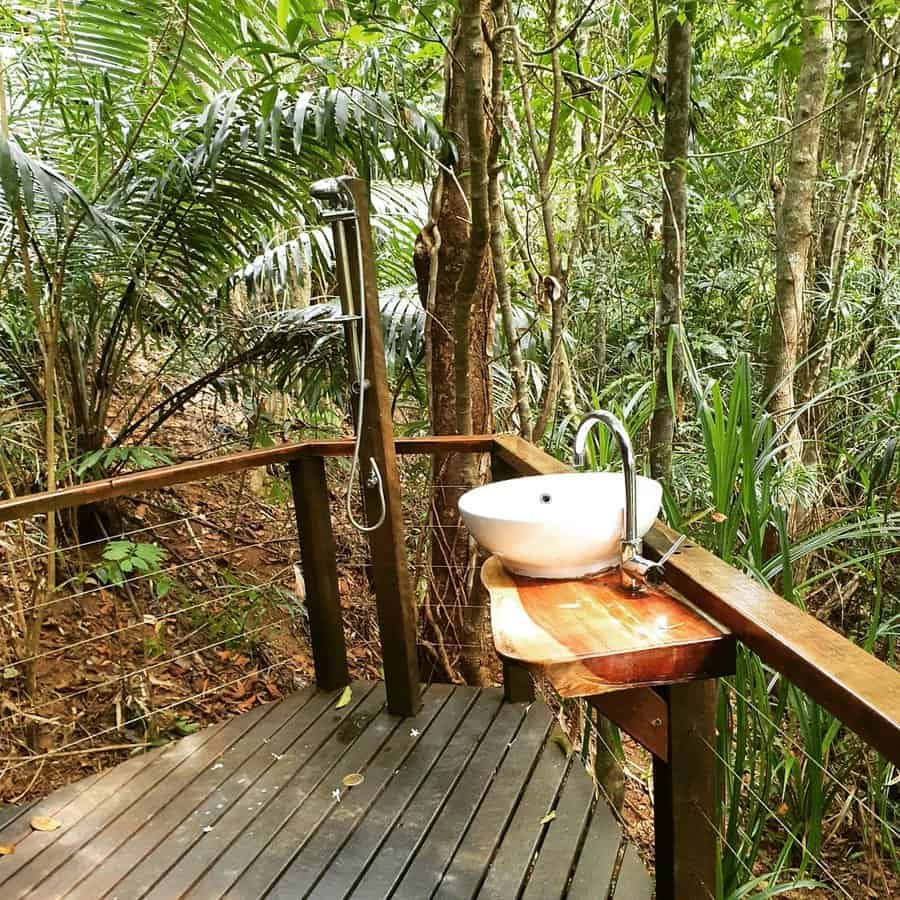 Outdoor shower and sink on a wooden deck surrounded by lush green forest