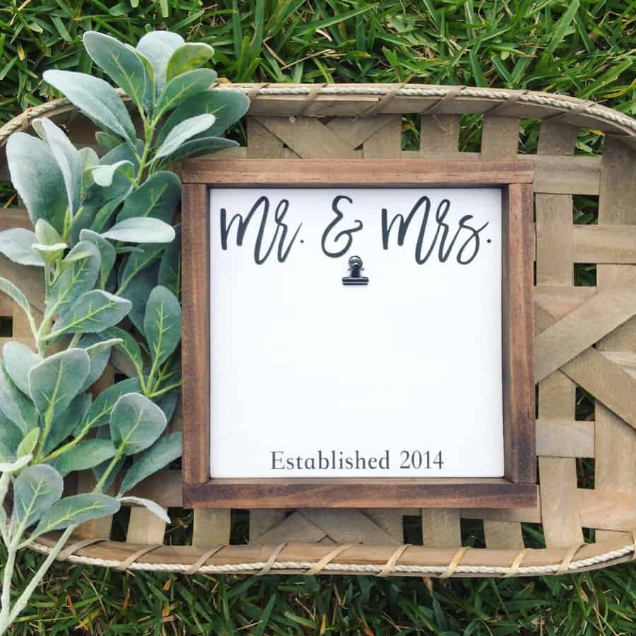 A wooden frame with "Mr. & Mrs." and "Established 2014" on white paper, placed in a woven basket 