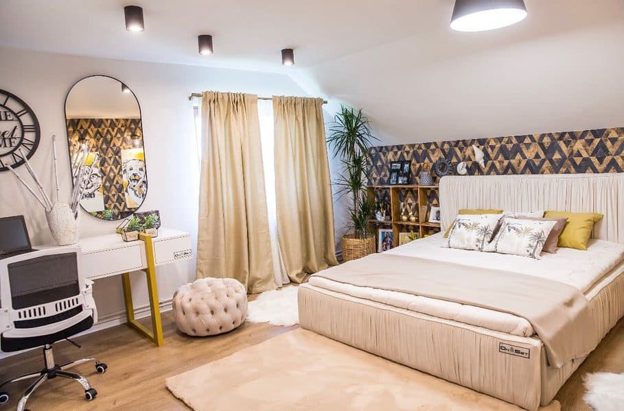 Stylish attic bedroom with warm neutrals, geometric wallpaper, and a cozy workspace, creating a chic and functional retreat.