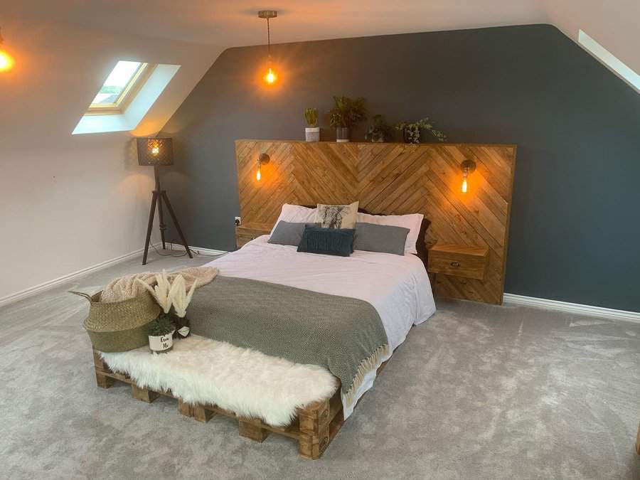 Modern attic bedroom with a bold dark accent wall, rustic wood headboard, warm lighting, and cozy textures for a stylish and inviting space.