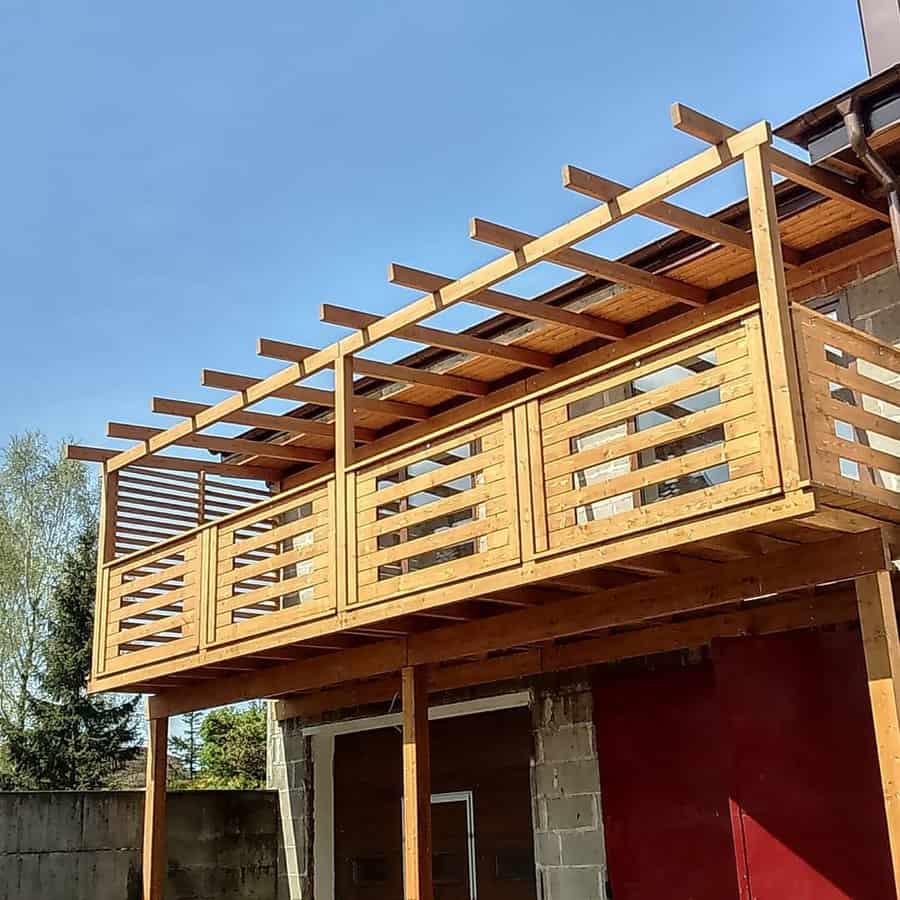 Wooden balcony with slatted railings and pergola roof, attached to a building