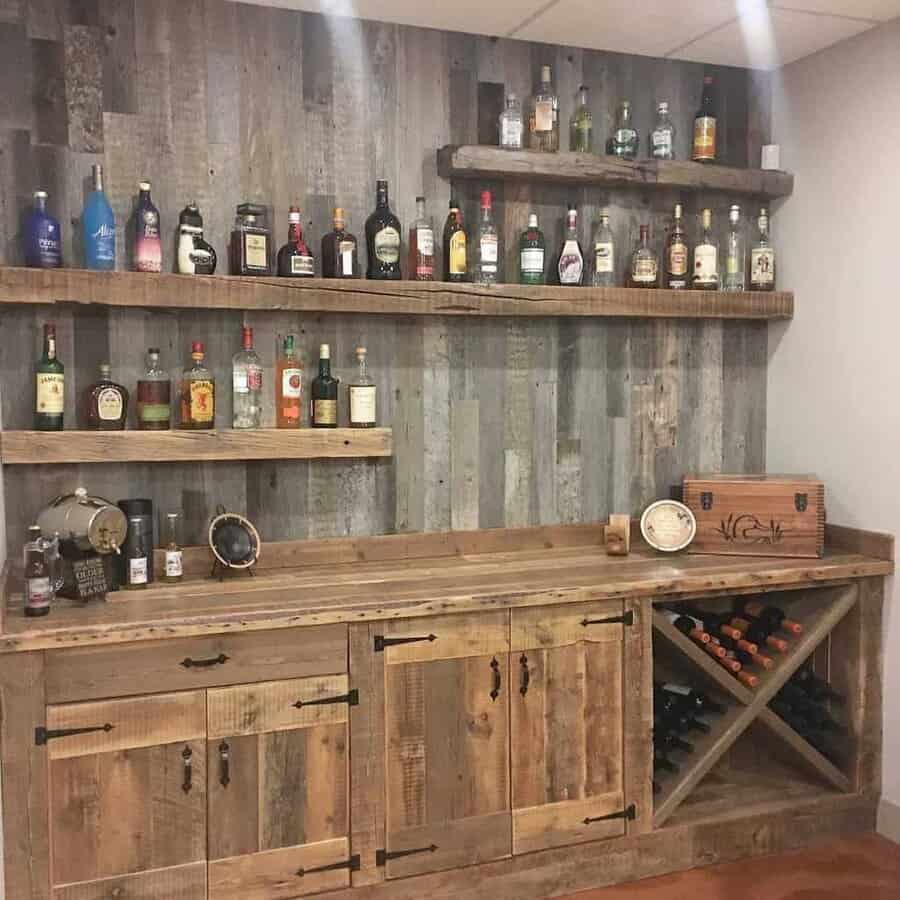 Rustic home bar with wooden shelves displaying various liquor bottles; wine rack and decorative items on wooden cabinet below