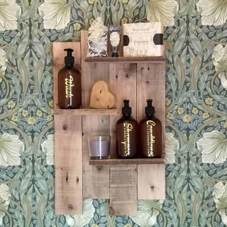 Wooden shelf with amber bottles, a heart-shaped stone, a candle, and packaged items against floral-patterned wallpaper