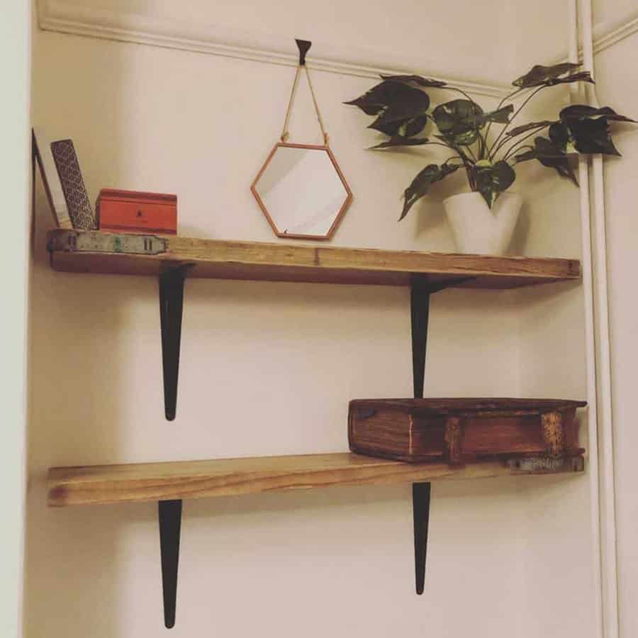 Two wooden shelves with metal brackets holding a potted plant, a hexagonal mirror, books, and a small red box