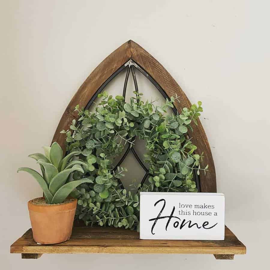 A wooden shelf with a potted plant, a leafy wreath, and a sign reading "Love makes this house a home"