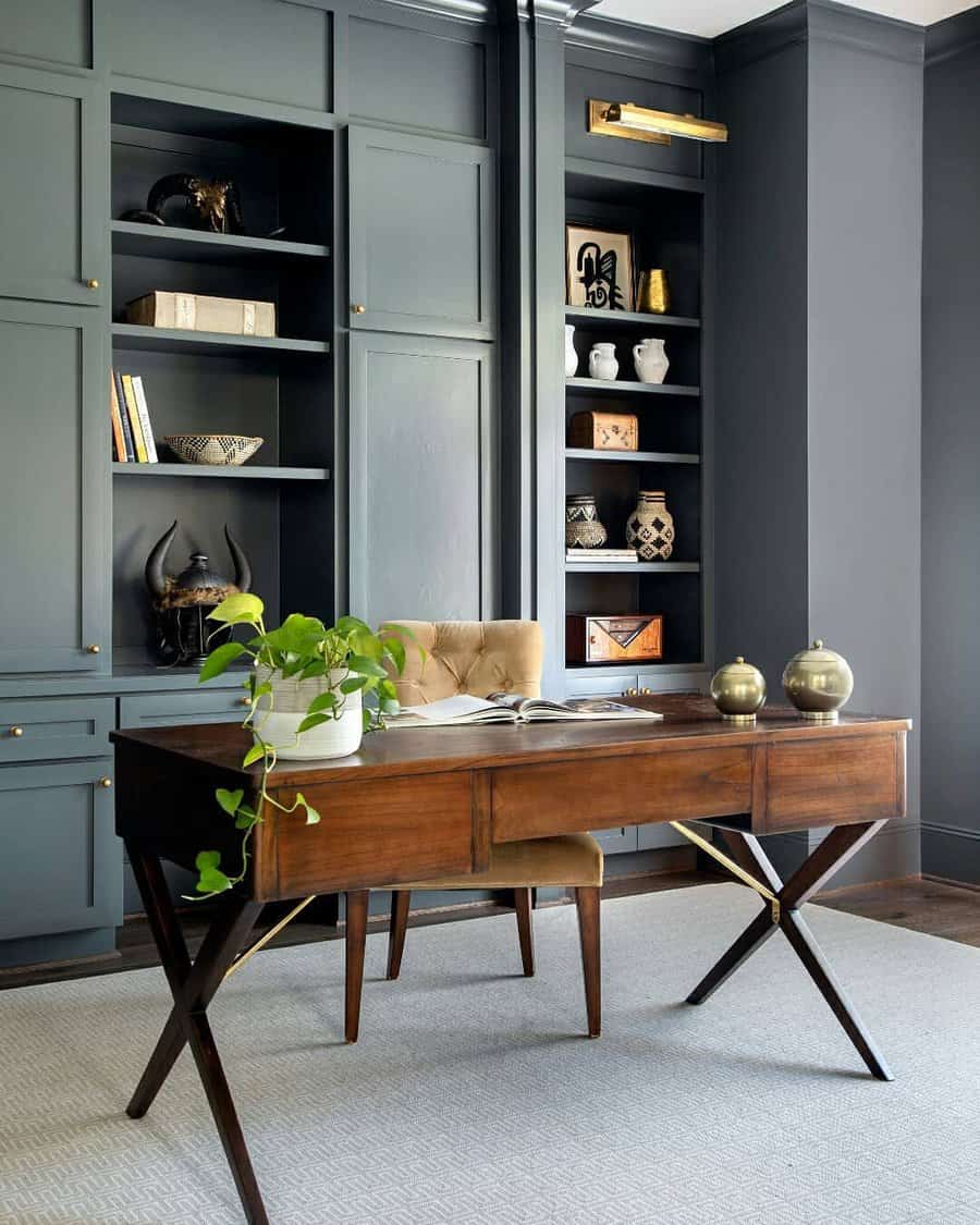 A stylish home office with dark built-in shelves, a wooden desk, a beige chair, and decorative items, including plants and globes