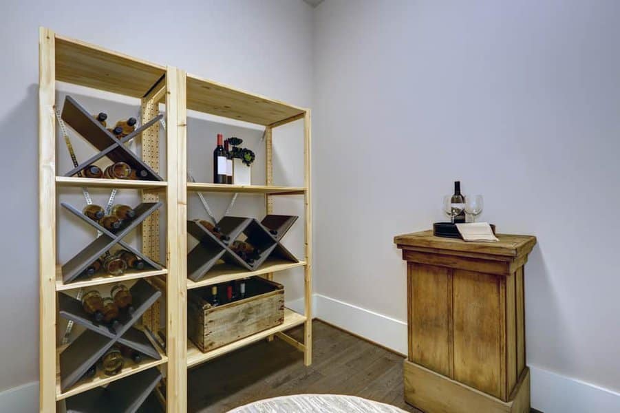 Small wine cellar with wooden racks holding various wine bottles, a crate, and a wooden stand with wine glasses and a bottle