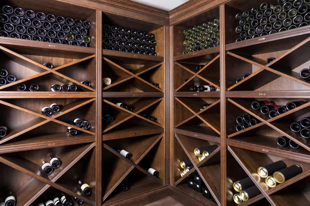 Wooden wine cellar with diagonal shelves filled with rows of wine bottles in a corner