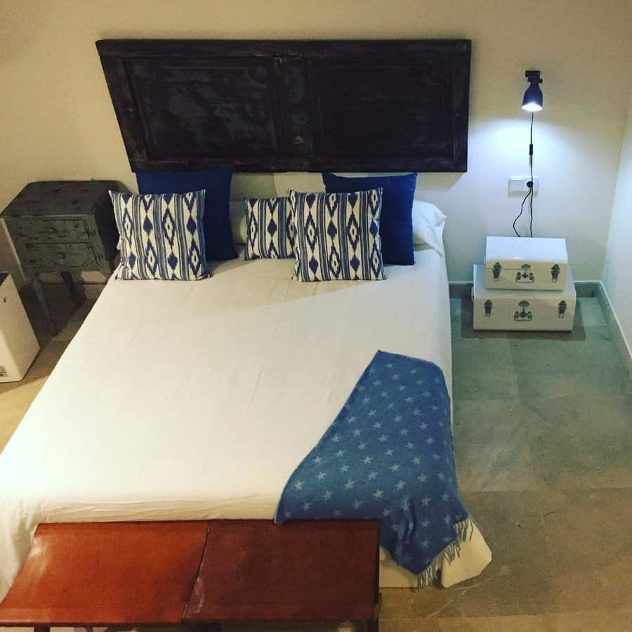 A neatly made bed with blue and white pillows, star-patterned blanket, a dark wooden headboard, and a nightstand with a lamp