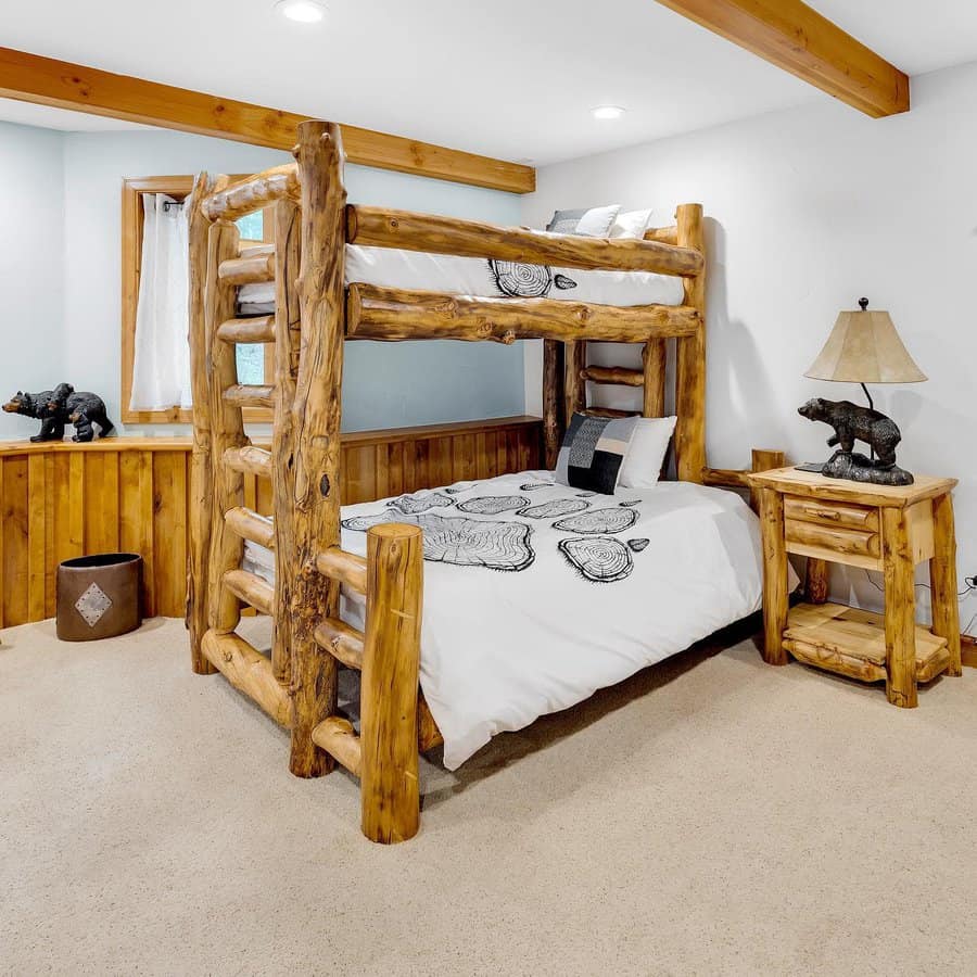 Rustic bedroom with wooden bunk beds, log headboard, animal-themed bedding, bedside table with lamp, and bear decorations; cozy carpeted floor