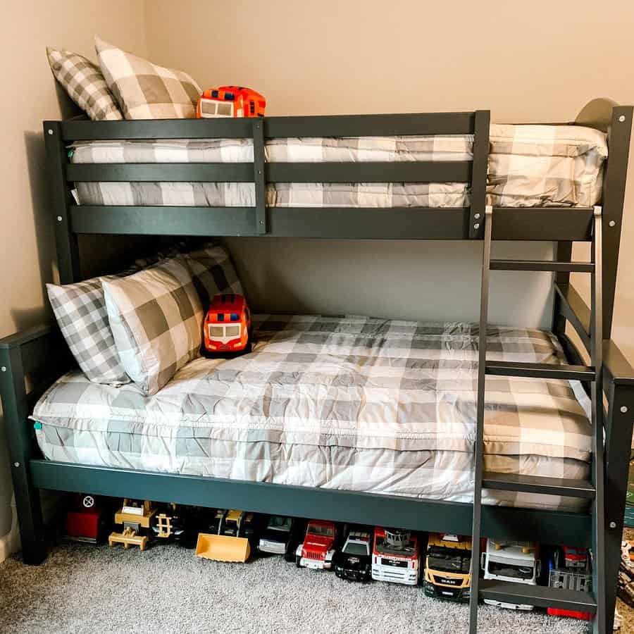 A gray bunk bed with plaid bedding, a ladder, and toy trucks lined up underneath in a cozy room