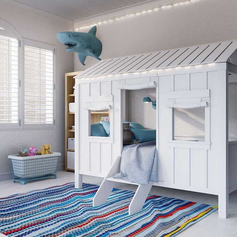 Children's room with a playhouse bed, blue and white decor, plush shark on the wall, and a colorful striped rug