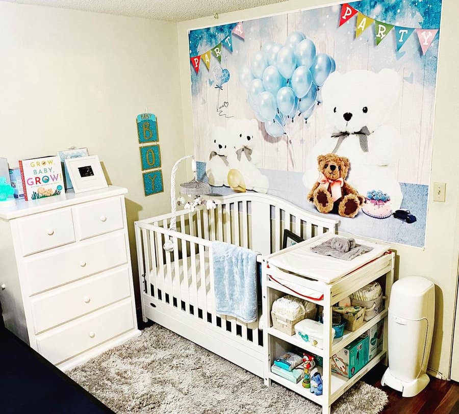 Bright nursery with crib, changing table, and dresser; Teddy bear mural with balloons on the wall, and books and decor on the dresser