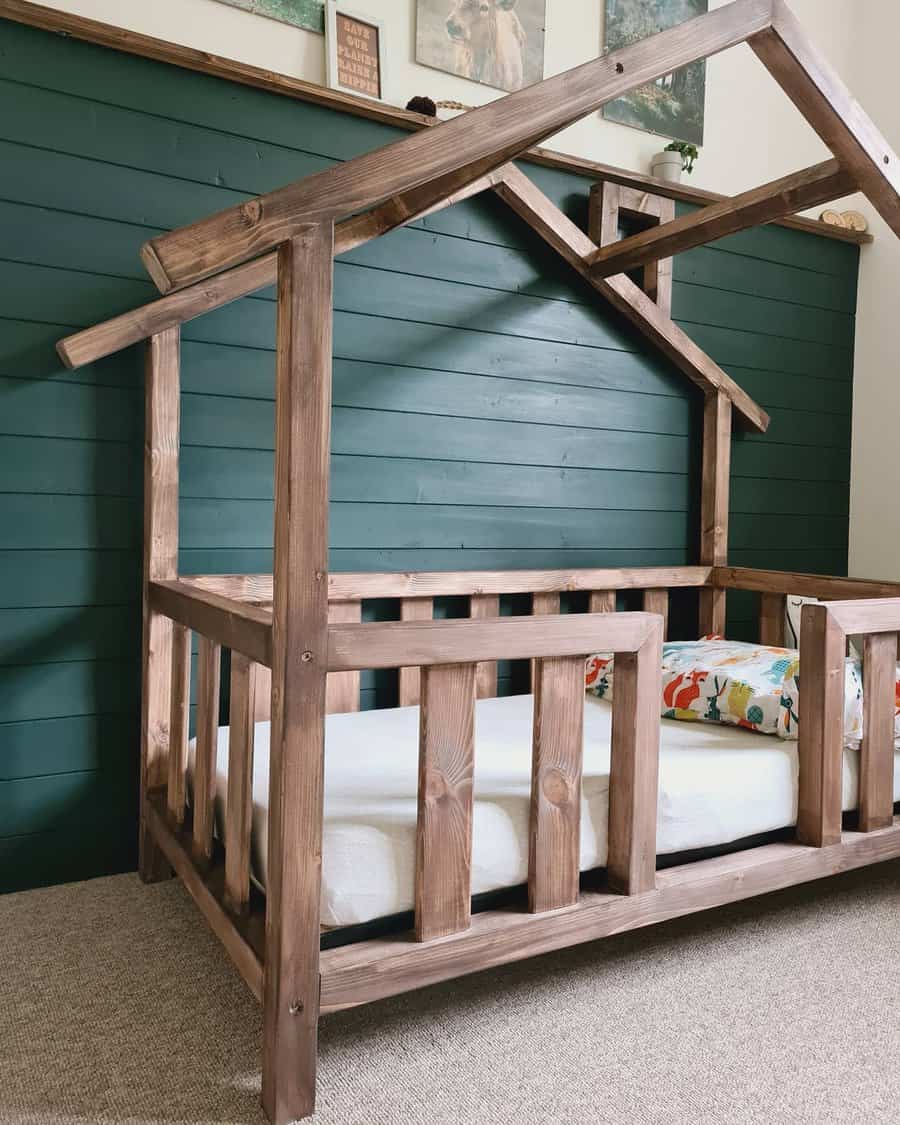 Wooden house-shaped bed frame with a mattress, set against a green paneled wall, pillow with colorful animal print