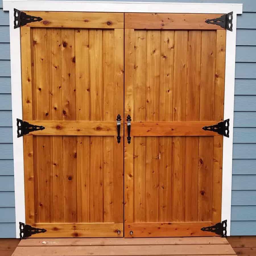 Wooden double doors with decorative black hinges set against a blue siding wall