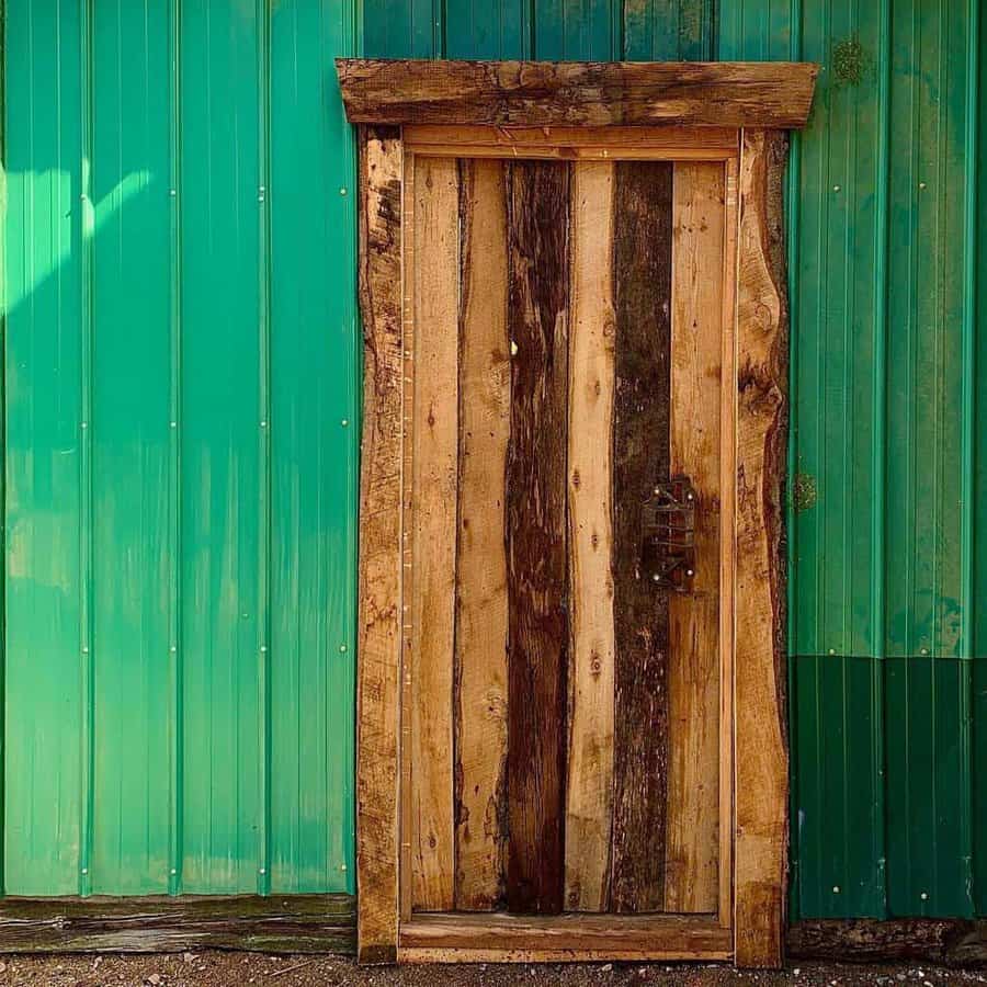 Rustic wooden door with varied planks set in a teal corrugated metal wall, casting a shadow on the ground